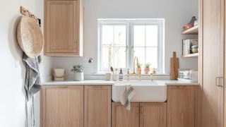 A calm and airy utility room with pale oak cabinetry, a traditional Belfast sink, and soft brass fixtures