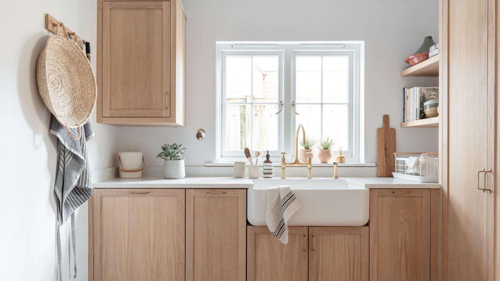 A calm and airy utility room with pale oak cabinetry, a traditional Belfast sink, and soft brass fixtures