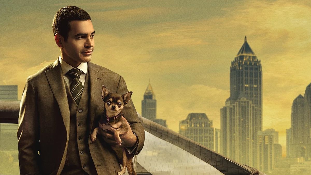 Will Trent (Ramón Rodríguez) leans on a car while holding his dog Betty (Bluebell) in front of the Atlanta skyline in a promo image for Will Trent season 2