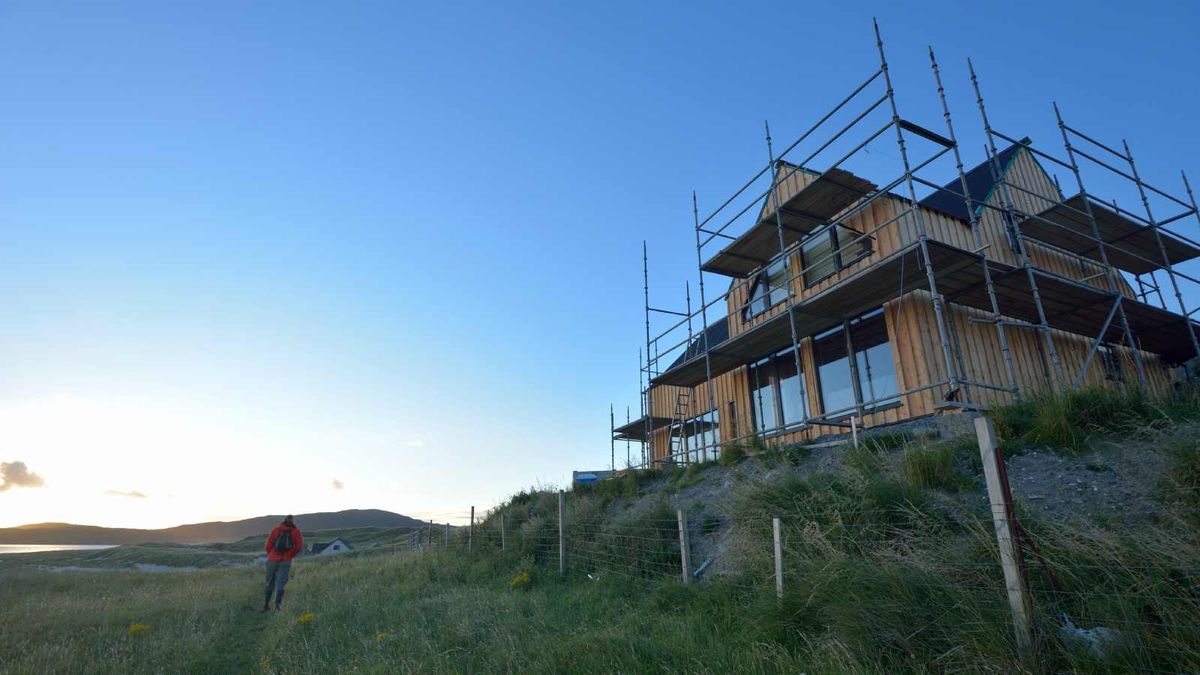 A modern timber-clad self build house under construction and surrounded by scaffolding overlooking the Scottish coastline