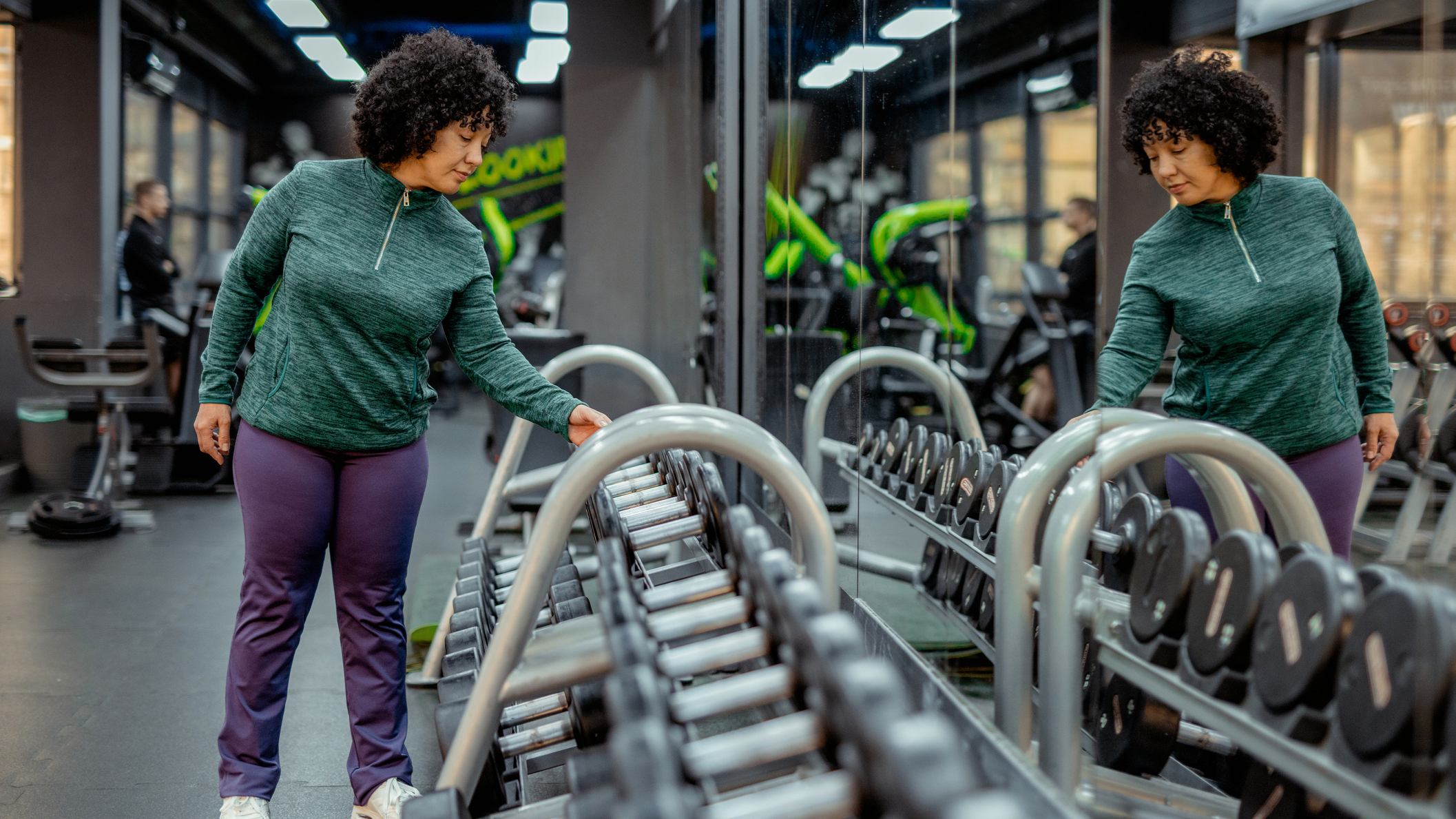 Woman in gym reaches for a dumbbell from a dumbbell rack