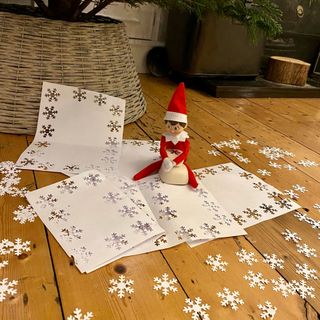 elf on the shelf with snowflakes cut out of white paper with hole punch