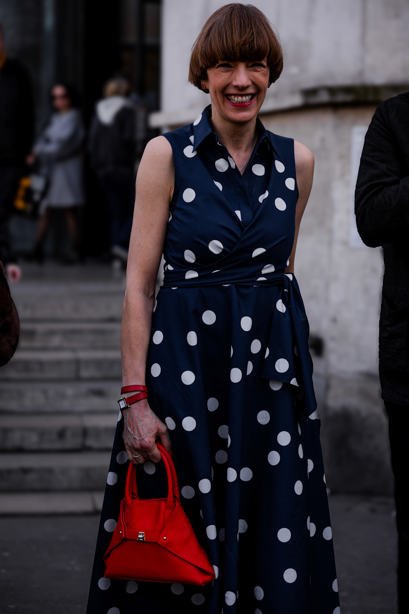 a woman in a black and white polka dot dress with a red bag and a bob haircut