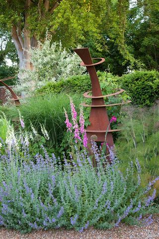 the steel sculpture is one of three designed by Ian Kitson and is underplanted with catmint and self-sown pink and white foxgloves