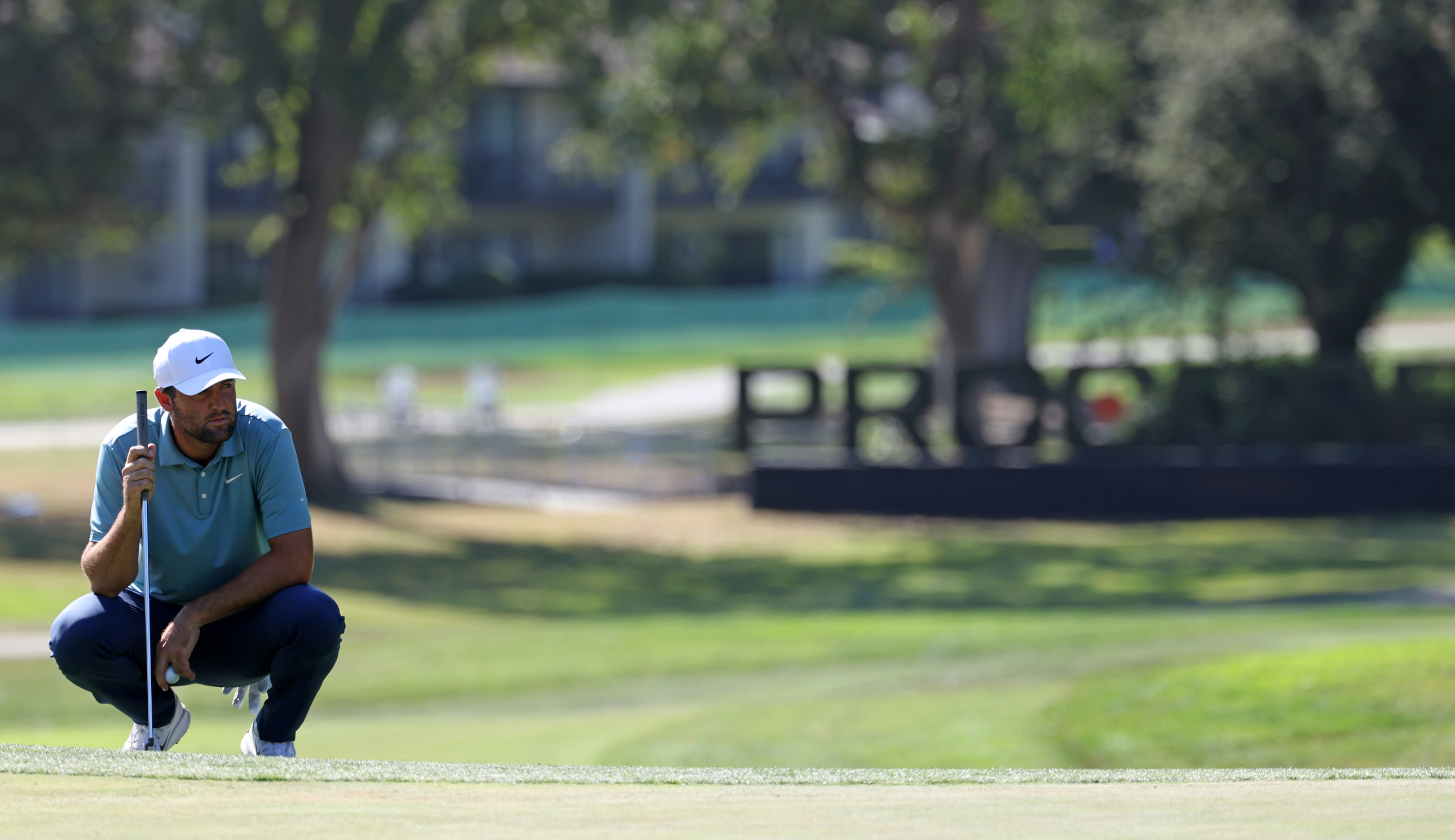 Scottie Scheffler lines up a putt in front of a Procore banner