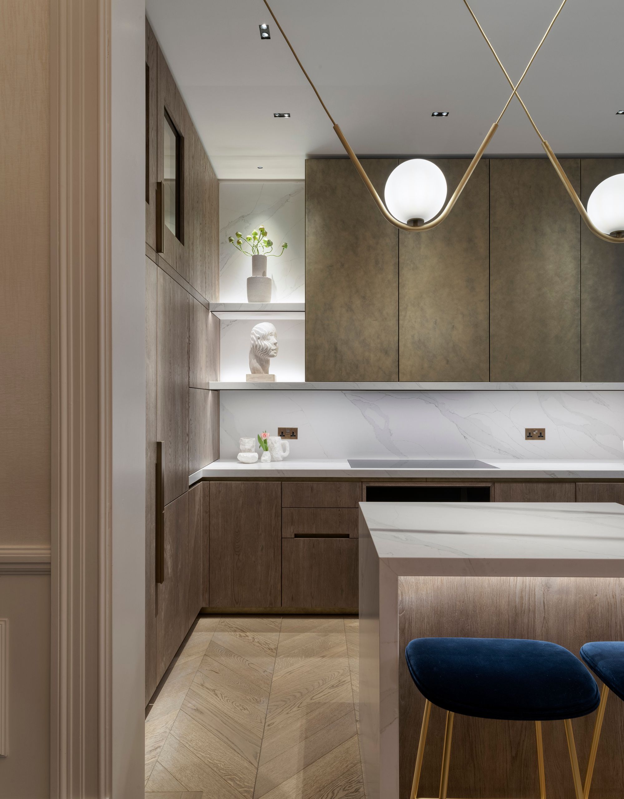 a modern kitchen with bronze cabinetry, white marble surfaces, hanging pendant lights and under-cabinet lighting