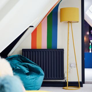 White painted wall with multi-coloured stripe design feature with black radiator and yellow floor lamp