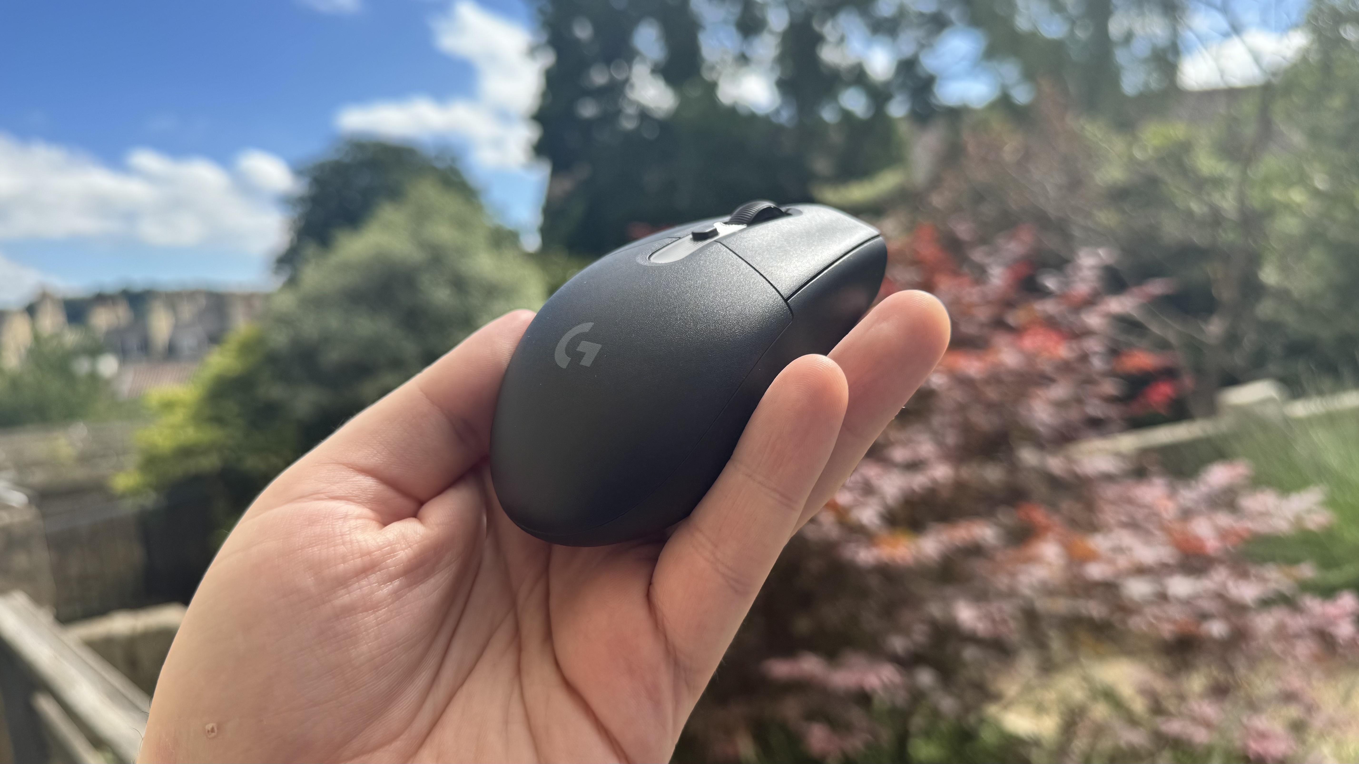 Logitech G305 X Superlight gaming mouse, held in a hand outside