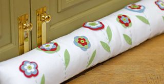Homemade draught excluder aginst a green door to show how to keep a house warm in winter