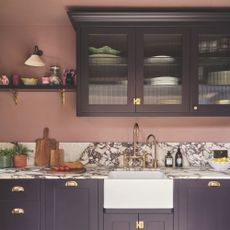 Kitchen with pink painted walls and purple cabinets, with a marble worktop and white ceramic sink