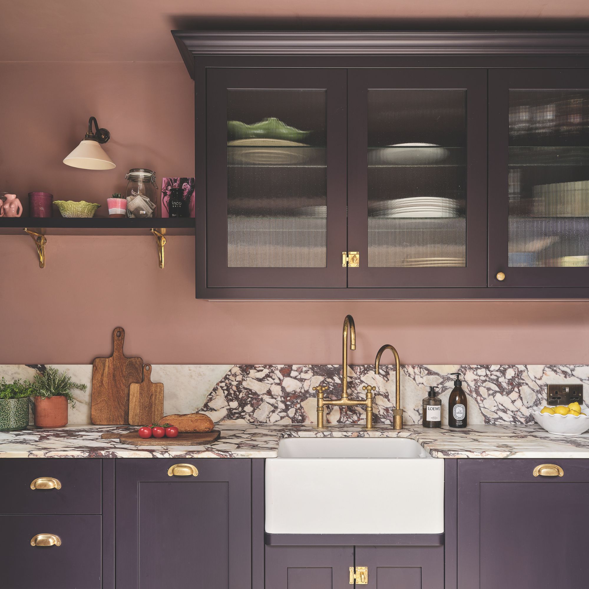 Kitchen with pink painted walls and purple cabinets, with a marble worktop and white ceramic sink