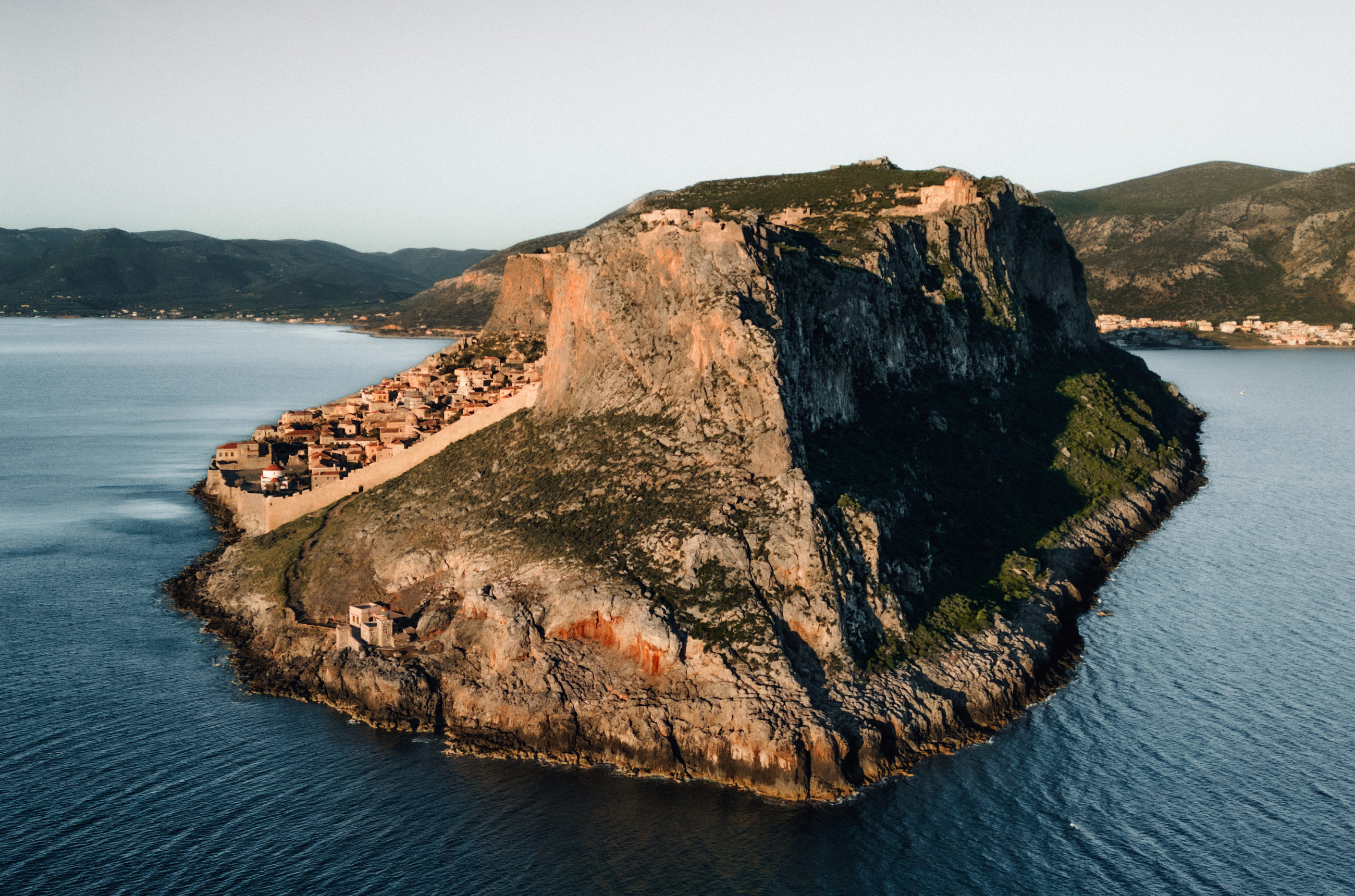 Large steep cliff face surrounded by water with a town on the left