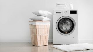 A washing machine with two pillows stacked on a laundry hamper next to it