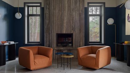 a living room with two orange armchair and gold flos lighting