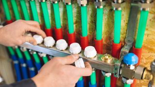 Hands on underfloor heating manifold with green, red and blue pipes