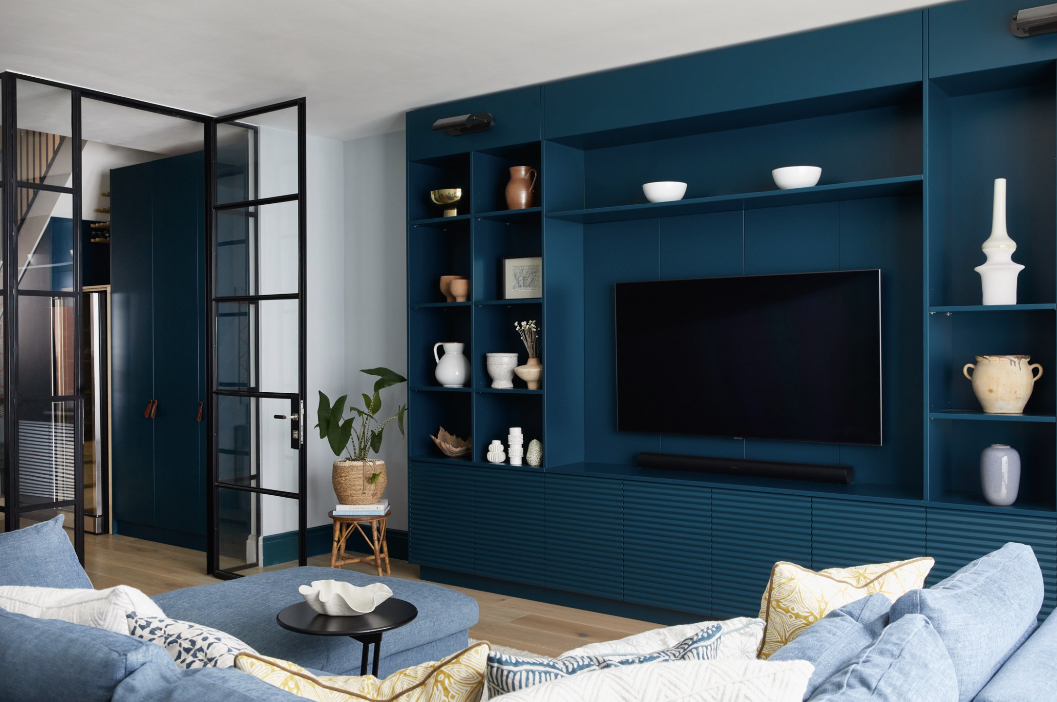 A contemporary living room with built-in media unit, combining open and closed shelving and painted a deep shade of blue
