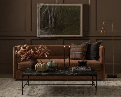 A living room with brown panelled walls, a brown sofa, and a coffee table with Halloween decor