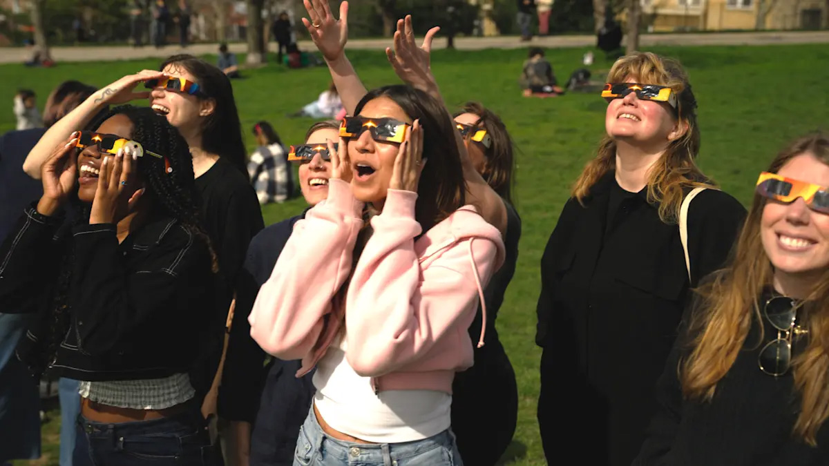 A crowd of people wearing solar glasses, looking up to the sky watching a solar eclipse
