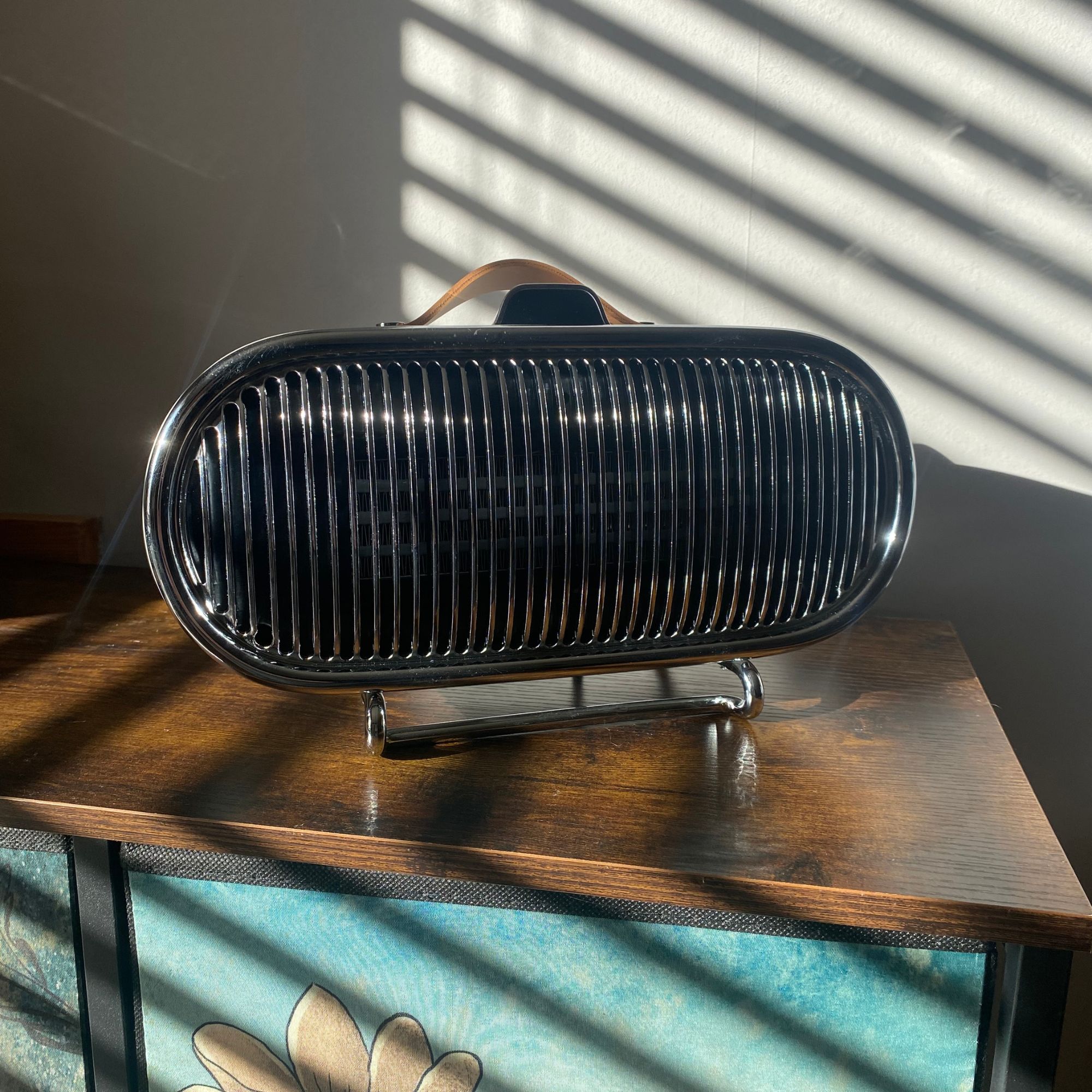 Swan 1.5kW Retro Ceramic Heater sitting on a sideboard with sunlight bouncing off the chrome grille