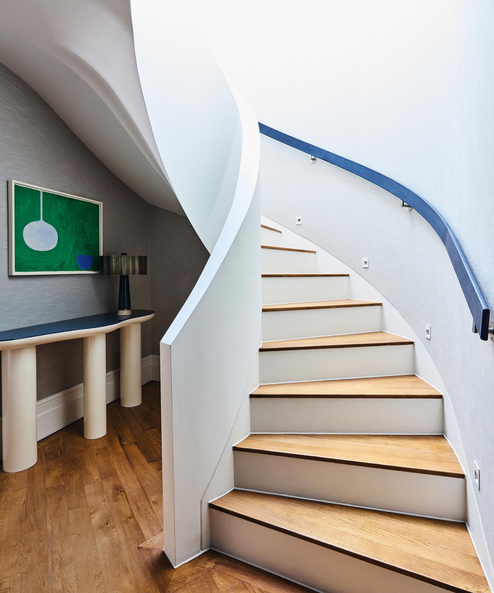 a white curved staircase with wooden treads, a blue curved handrail and a white and blue sculptural hall table