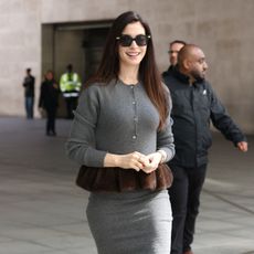 An image of Anne Hathaway wearing a grey knit with spring skirt.