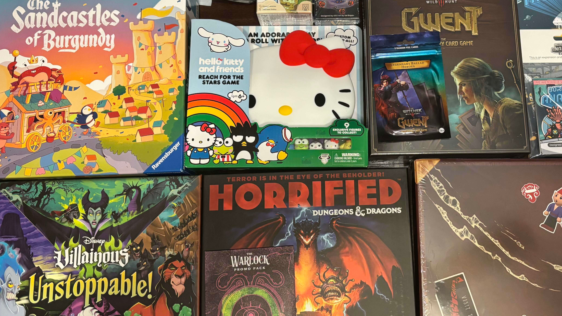 A collection of board games laid out face-up, including The Sandcastles of Burgundy, Gwent, Disney Villainous Unstoppable, Dungeons &amp; Dragons Horrified, and Triangle Agency