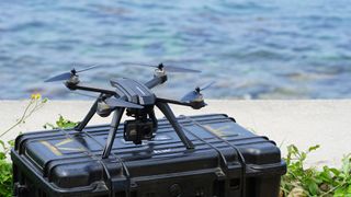 The Potensic D85 camera drone is sat on top of a black hard case flight case, positioned in front of a body of water