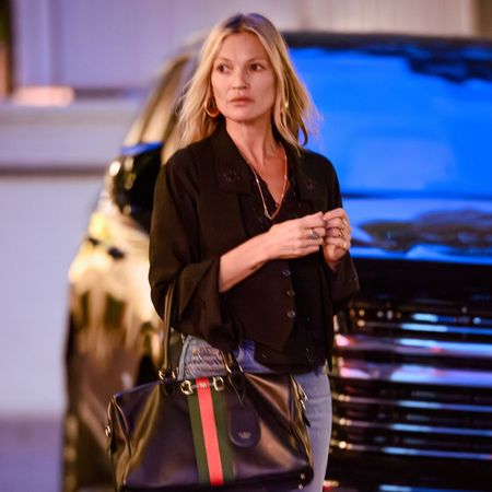 Kate Moss steps outside wearing stove pip jeans with heeled boots and a black blouse.