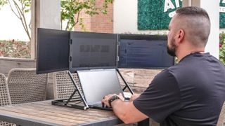 A person working on the Aura Triple Aero 15.6 Pro Max portable monitor with a laptop on a table outside at a coffee shop