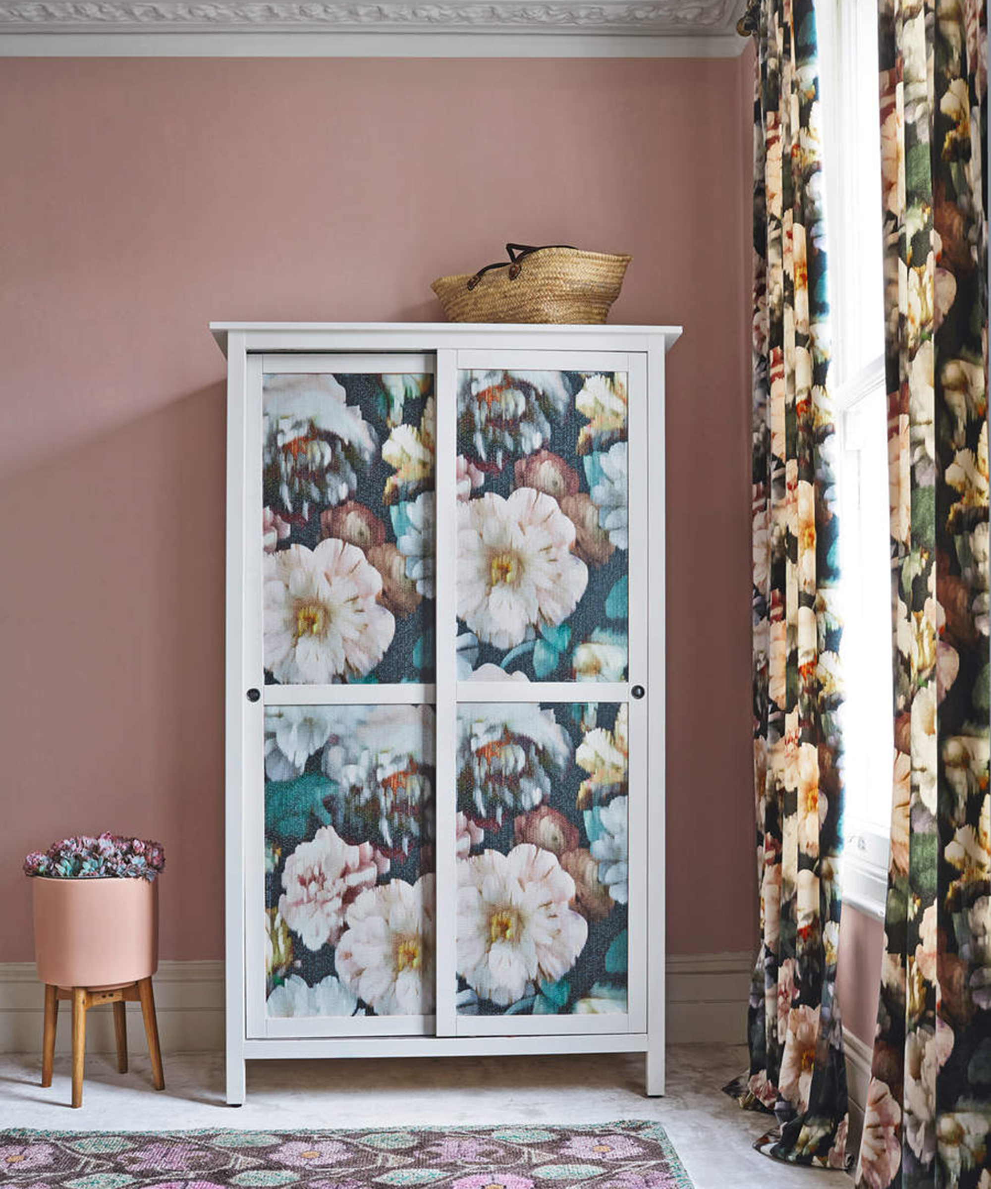 Wardrobe with panels decorated with large floral print against a pink wall with elaborate coving, floral curtains and rug.