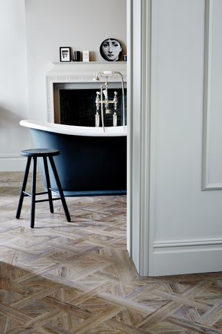 bathroom with Versailles style vinyl wood effect floor, black painted roll top bath, stool, artwork
