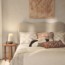 Cream bedroom with abstract art on wall, wavy head board and natural coloured bedding