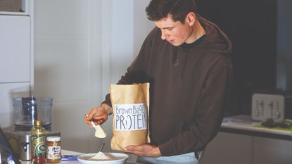 Male cyclist adding protein powder to a bowl to make energy bars at home