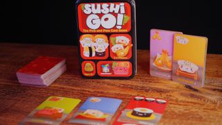 Sushi Go! cards and tin laid out on a wooden table