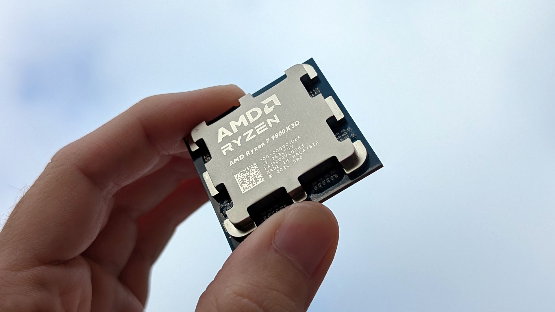 AMD Ryzen 7 9800X3D processor held in front of a blue cloudy sky