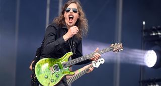 Mikael Åkerfeldt pulls a face while playing his green PRS Custom 24 live onstage at Tons of Rock 2024 with Opeth. He wears gold aviators and a black shirt. 