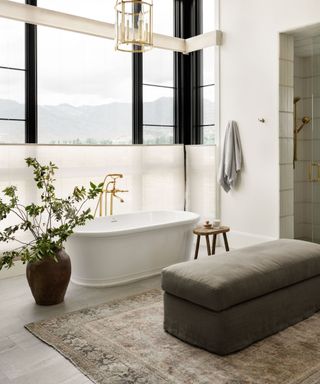 Freestanding bathtub with rug in front and upholstered ottoman