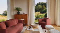 living room with a burnt amber sofa and accent chair, floor to ceiling windows, and long ivory drapes