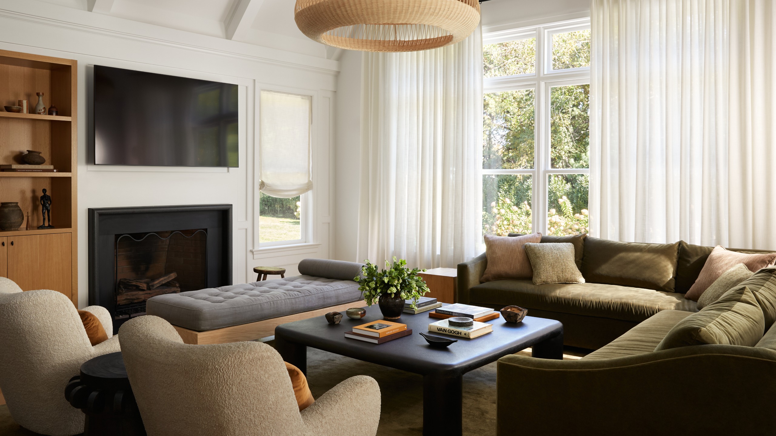 White living room with olive green velvet corner sofa, two beige armchairs, black square coffee table, grey ottoman and black fireplace