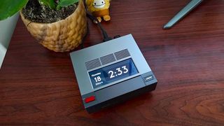 Ayaneo Mini PC AM02 on desk next to plant and bigfoot Squishmallow with time on built-in screen.