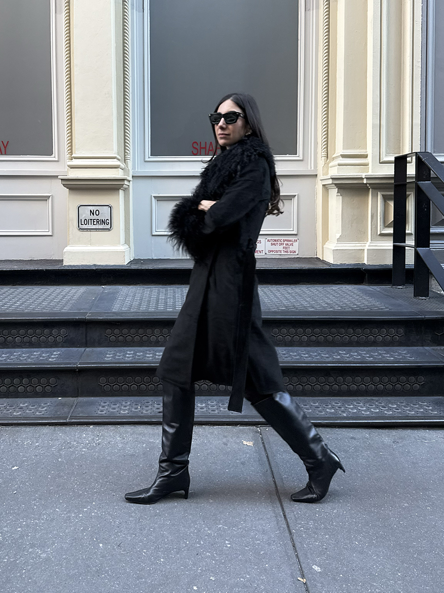 Melanie Masarin Ghia Founder Walking on Street Wearing All Black Winter Outfit With Boots, Sunglasses, and Furry Coat