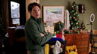 A still from the movie Christmas at the Chalet in which Brendan McRae as George stands in front of a Christmas tree