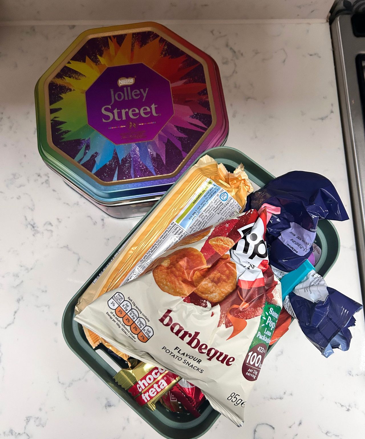 Messy snacks arranged in a green box and Quality Street tin