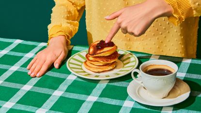 Woman having delicious breakfast with sweet pancakes and jam on green tablecloth. Vintage, retro style interior. Food pop art photography. Complementary colors. 