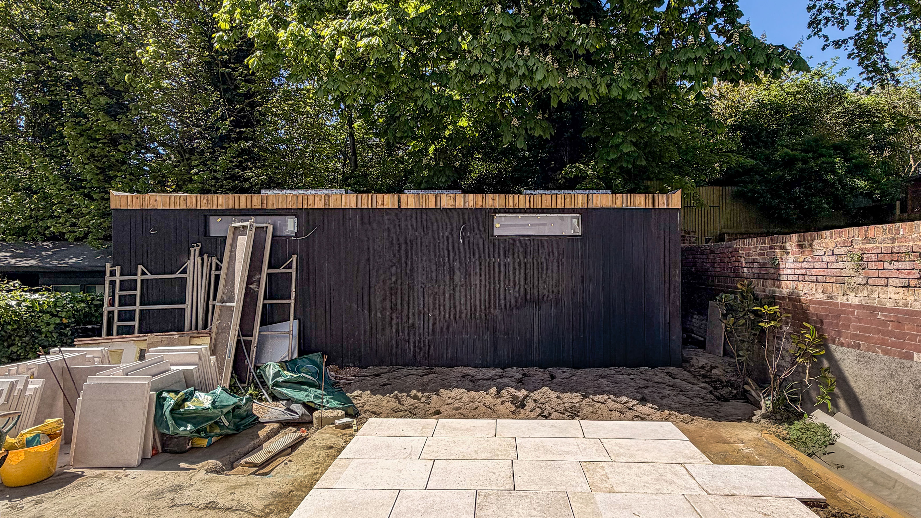 Summerhouse being built in front of trees in garden, with patio being paved in front