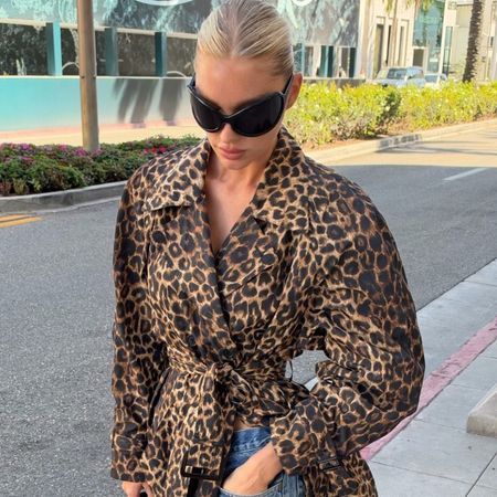 Elsa Hosk walks down the street wearing a leopard print trench coat with relaxed, slightly distressed jeans and navy satin mules.