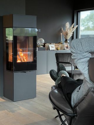 A person relaxing in a living room in front of a fireplace with an IKEA Eket bookshelf in the background