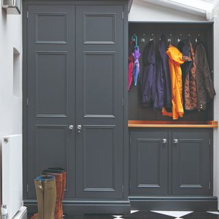 A hallway with a built-in blue wardrobe and coat hooks with jackets hung on them