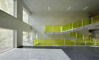Inside view of Campus Hoogvliet, Rotterdam, white tiled walls and ceiling, grey floor, white stairwell with lime green transparent panels, strobe ceiling lights, windows to the left letting in light, view of tree tops