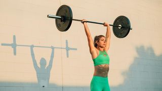 Woman outdoors holding a barbell above her head during workout